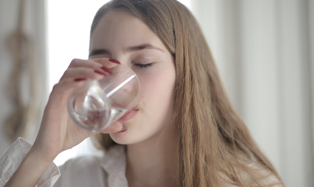無料 目を閉じて透明なガラスから水を飲む白いシャツの女性 写真素材