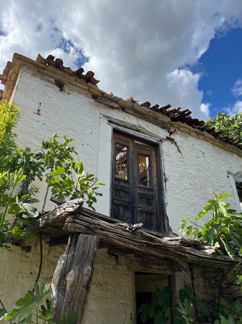 Free Sunlit view of a rustic Greek house with wooden details and lush greenery, under a bright blue sky. Stock Photo