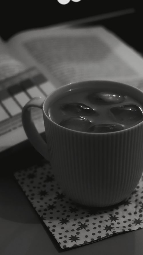 Free A warm cup of coffee next to an open book, in a black and white setting. Stock Photo