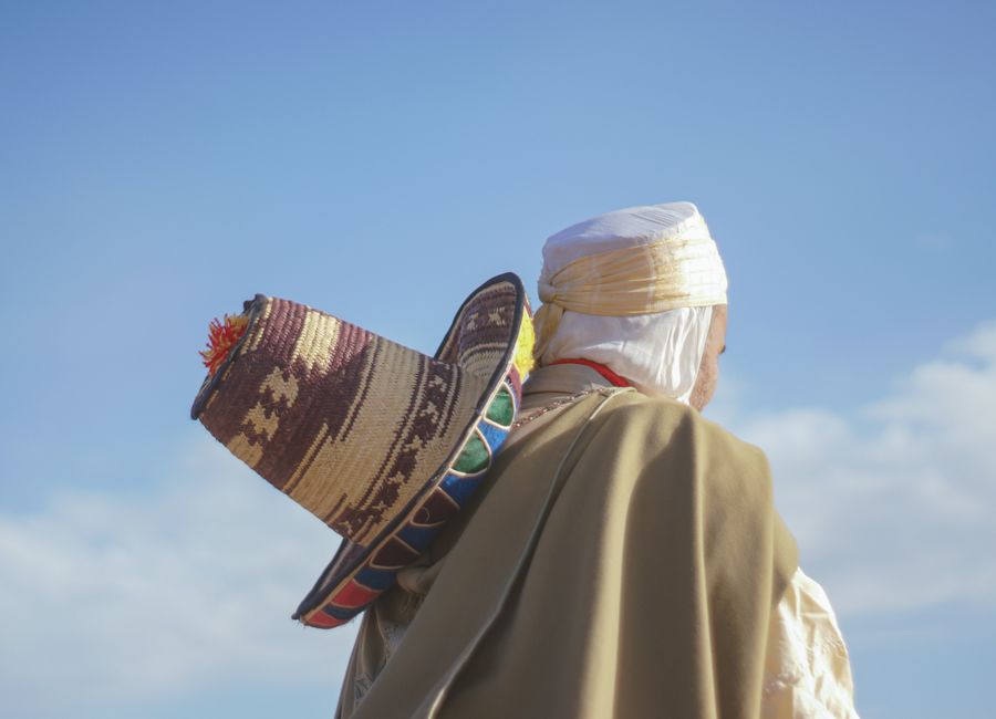 A man wearing traditional attire and a hat against a clear blue sky in Ain Merane, Algeria.