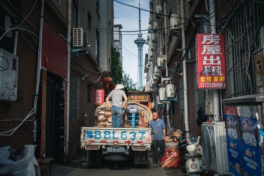 Street scene with workers unloading a truck in a narrow urban alley.