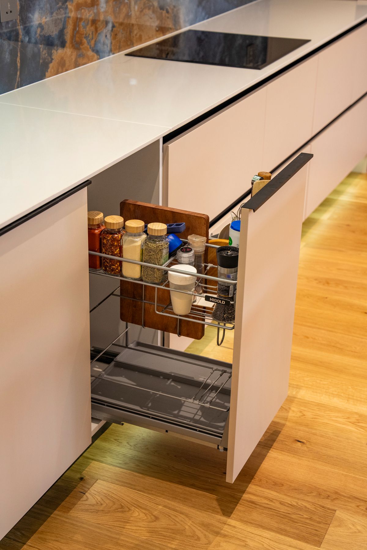 Close-up of a white modern kitchen with a black induction cooktop and a narrow pull-out cabinet containing spices and kitchen supplies.