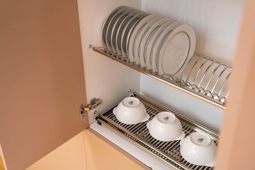 A clean and organized kitchen cabinet displaying plates and bowls on a drying rack.