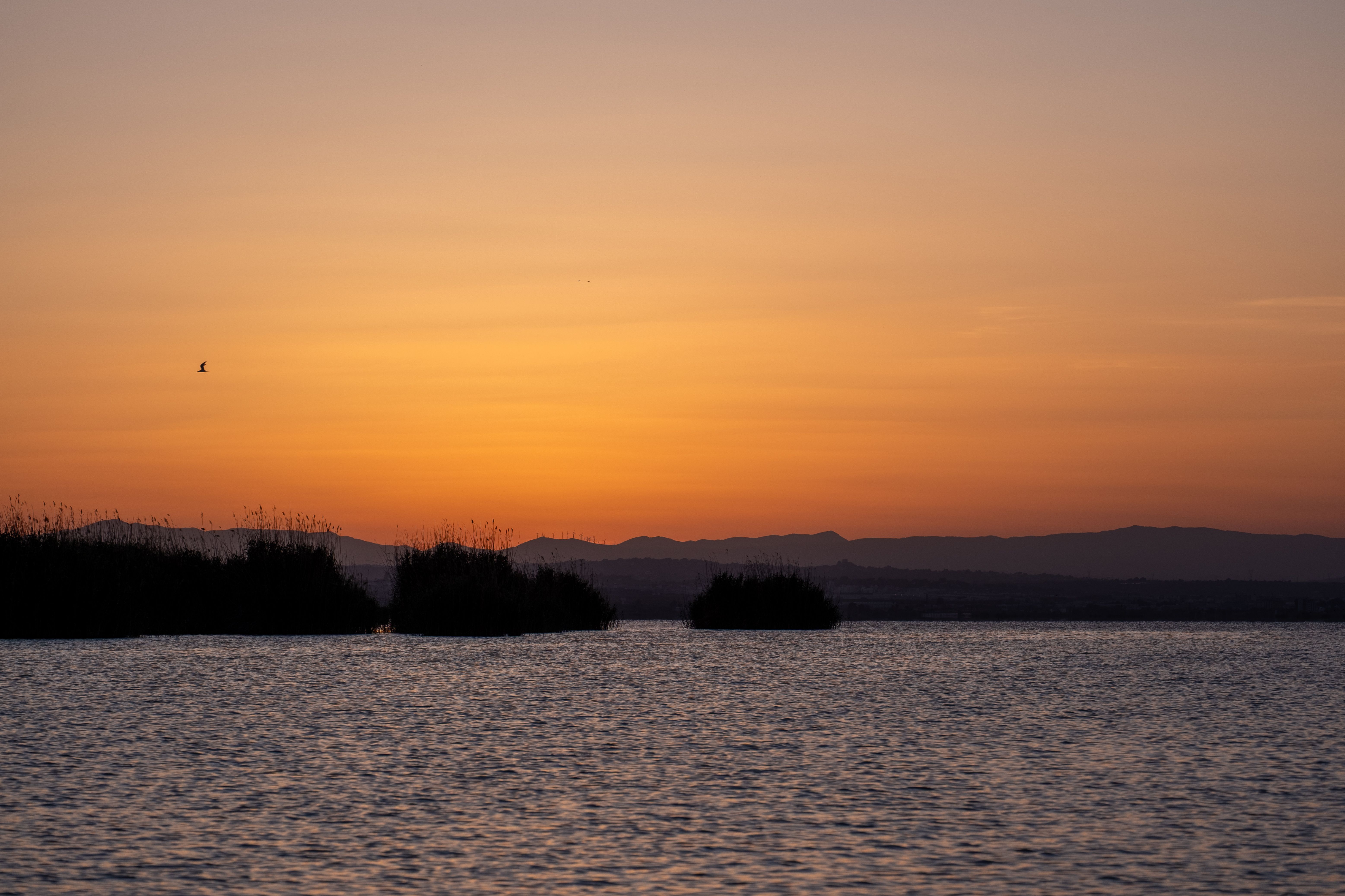 Breathtaking sunset over a calm lake with distant silhouettes under a vibrant sky.