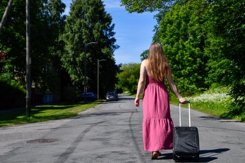 Traveller walking a tree-lined street with a rolling suitcase — photo by Margo Evardson on Pexels