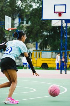 Young woman playing basketball outdoors on a court in Mexico City, showcasing athleticism and focus.