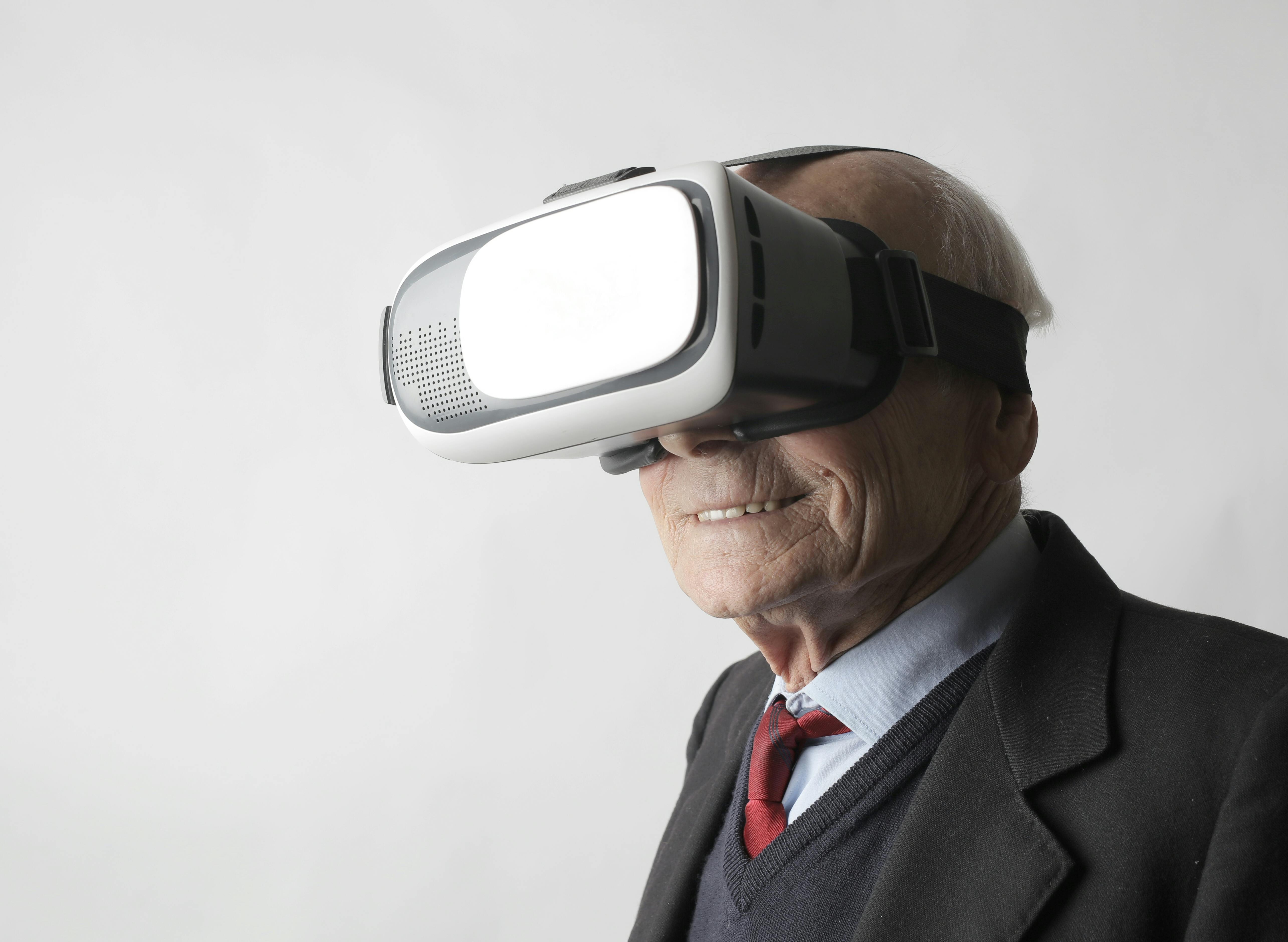 Smiling elderly gentleman wearing classy suit experiencing virtual reality while using modern headset on white background