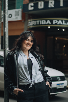 A woman smiles standing outdoors in front of Curitiba Palace, offering a warm urban vibe.