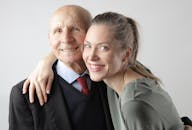 一位开朗的老人和一位成年女子在白色背景前拥抱，看着镜头