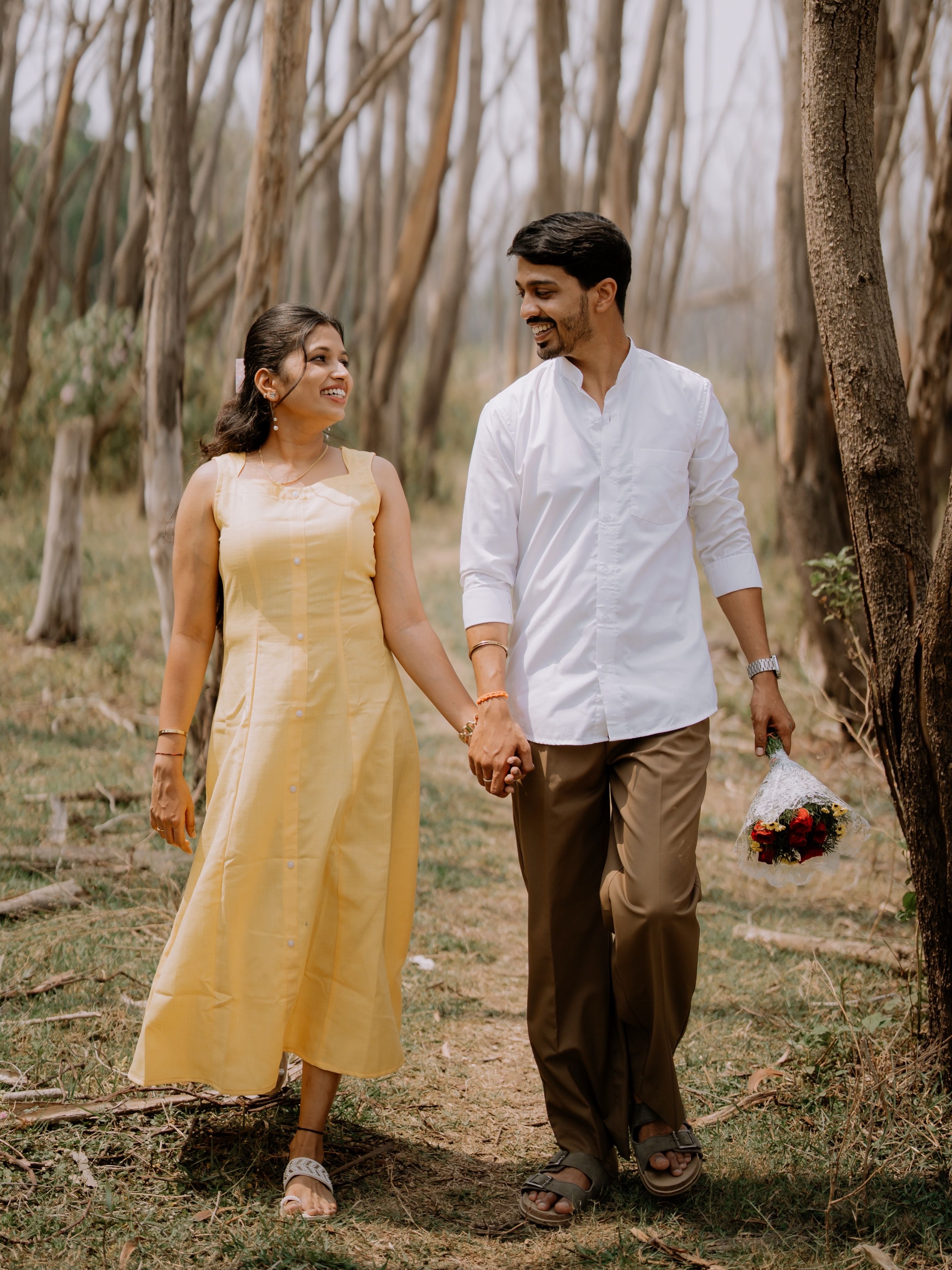 Couple enjoying a romantic walk hand in hand in a sunny forest setting.