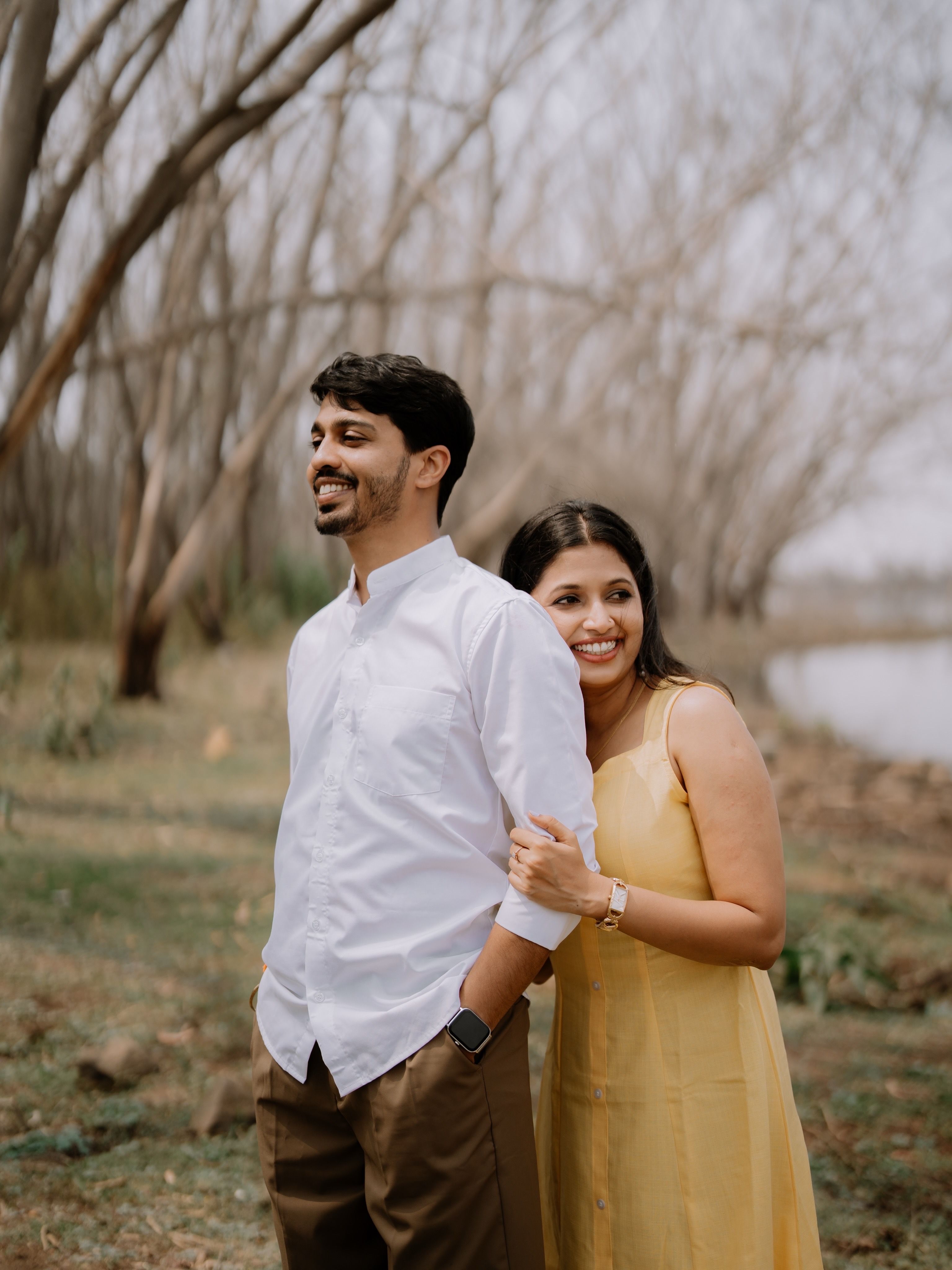Joyful couple embracing in a serene outdoor setting with trees and a lake in the background.