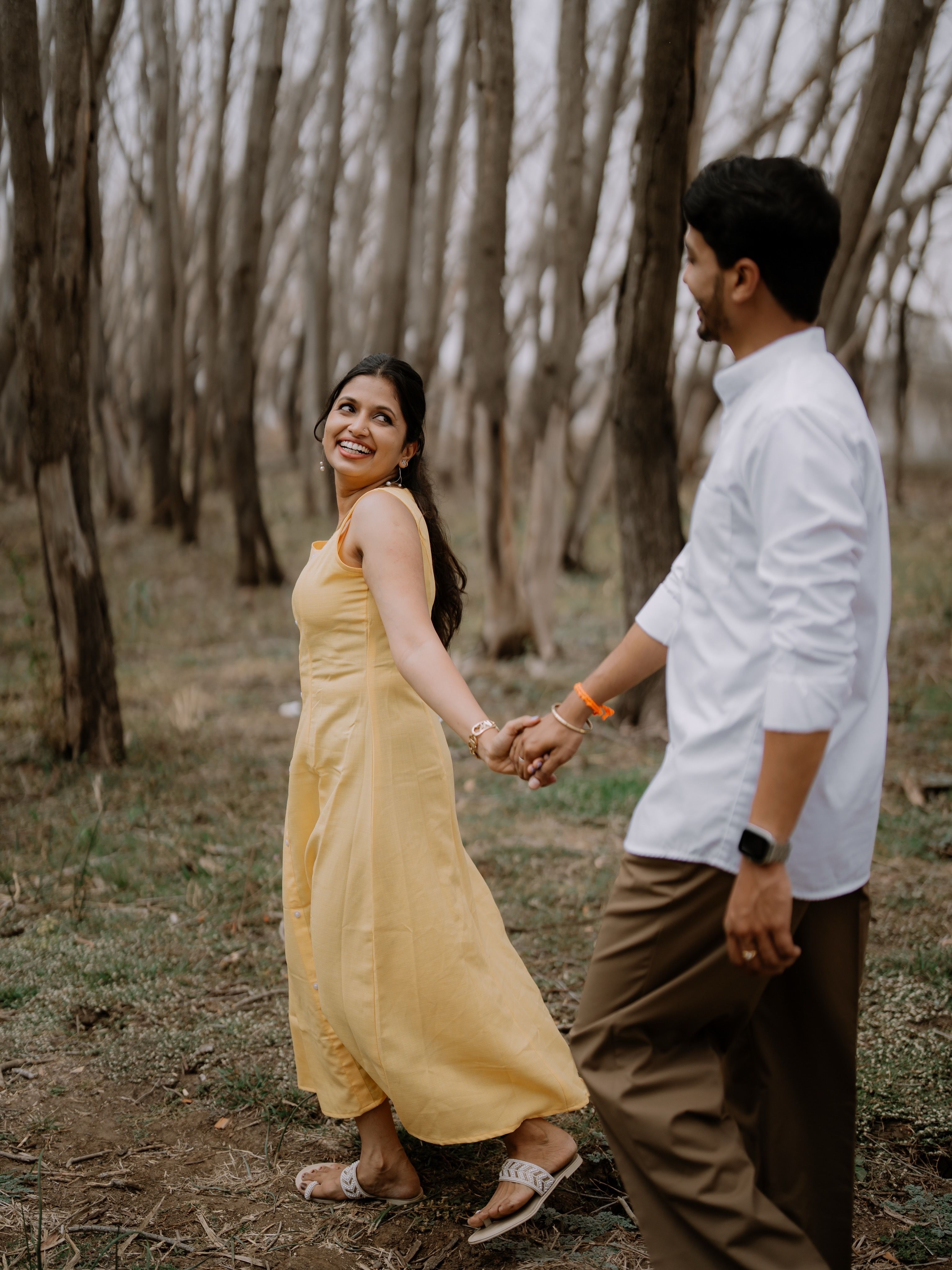 A joyful couple holding hands, walking through a serene forest in spring.