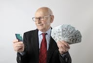 穿着西装的老人手持信用卡和美元钞票，象征着金融与财富