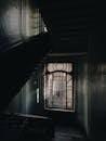 一张通过老式窗户照亮的黑暗楼梯照片，营造出一种令人毛骨悚然的氛围
