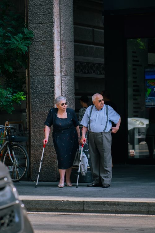 Free An elderly couple leans on crutches waiting to cross a city street during the day. Stock Photo