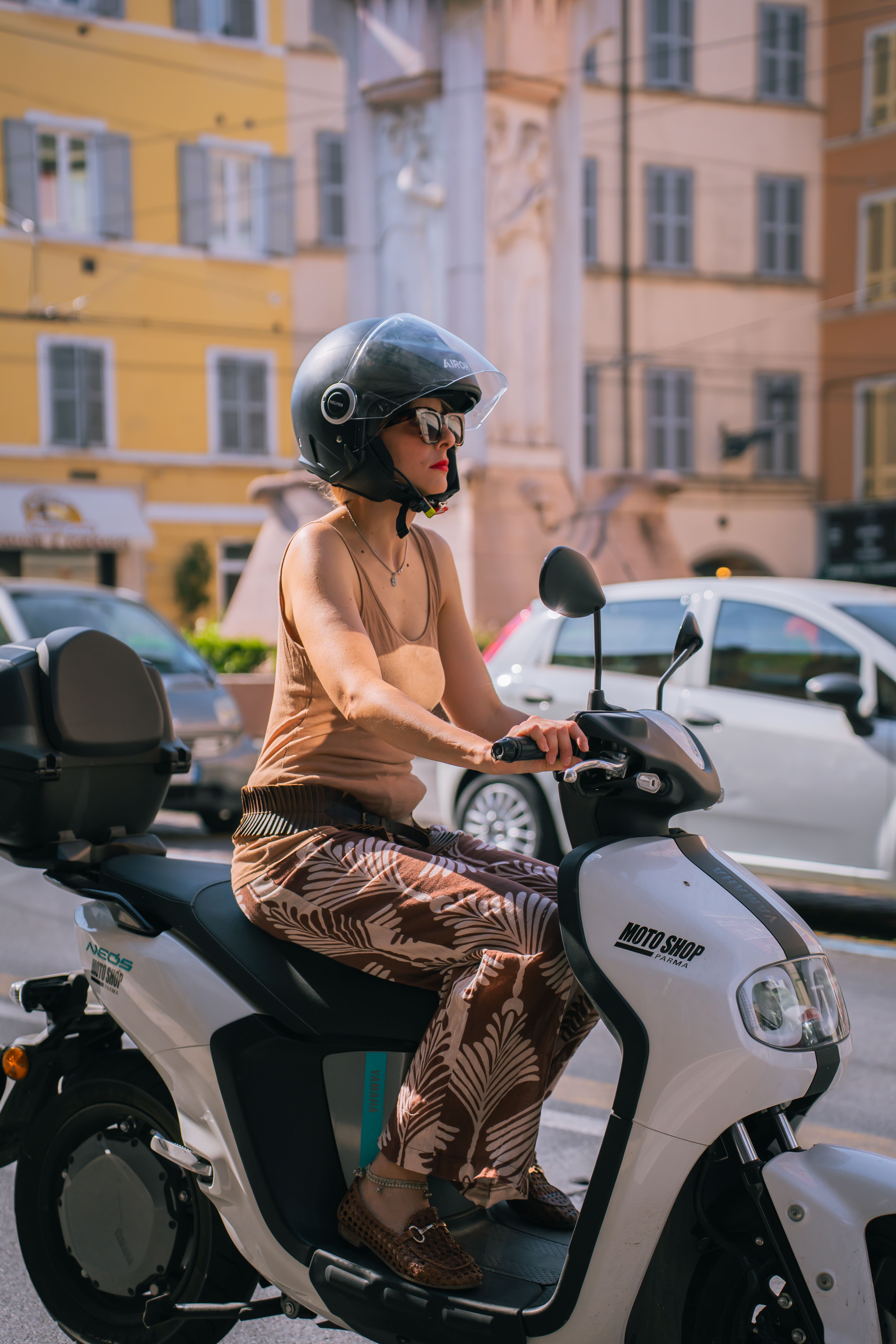 A woman wearing a helmet rides a scooter through a vibrant city street, showcasing urban lifestyle.