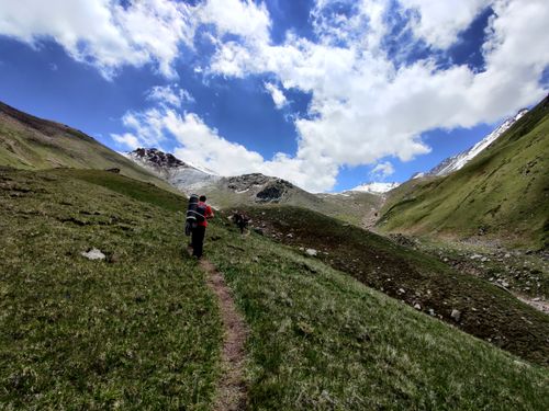 Free Hikers exploring the lush, green mountain trails of Almaty under a bright sky. Stock Photo