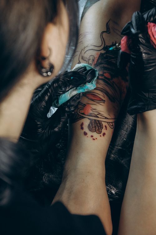 Free Tattoo artist creating a detailed design on a client's arm, showcasing precision and artistry. Stock Photo