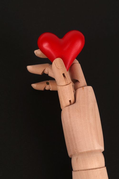 Free Wooden mannequin's hand holding a red heart against black background, symbolizing love and support. Stock Photo