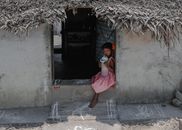 A young girl sits in a rural doorway in Kanchipuram, Tamil Nadu, sipping water on a sunny day.