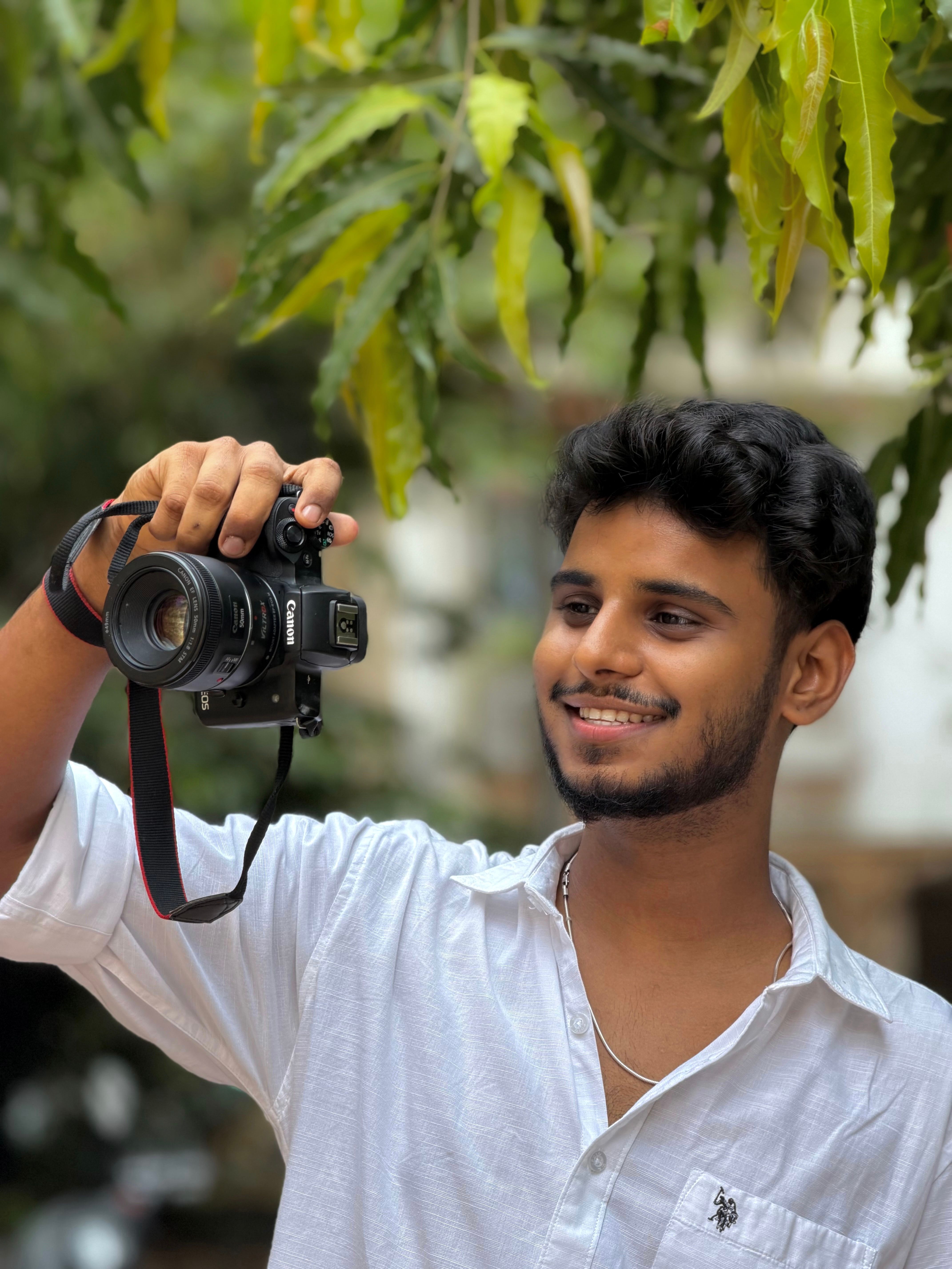 A young man taking photos with a digital camera surrounded by greenery on a sunny day.
