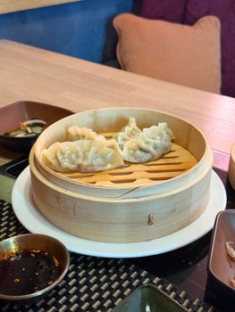 Appetizing steamed dumplings served in a bamboo basket with dipping sauce on a dining table.