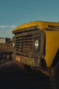 A vintage yellow truck with a worn exterior parked on a rural dirt road under a clear blue sky.