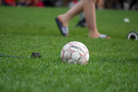 A close-up shot of a soccer ball on a green field, with blurred players in the background.