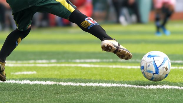 Dynamic close-up of a soccer player's foot as they kick a ball on a sunny field.