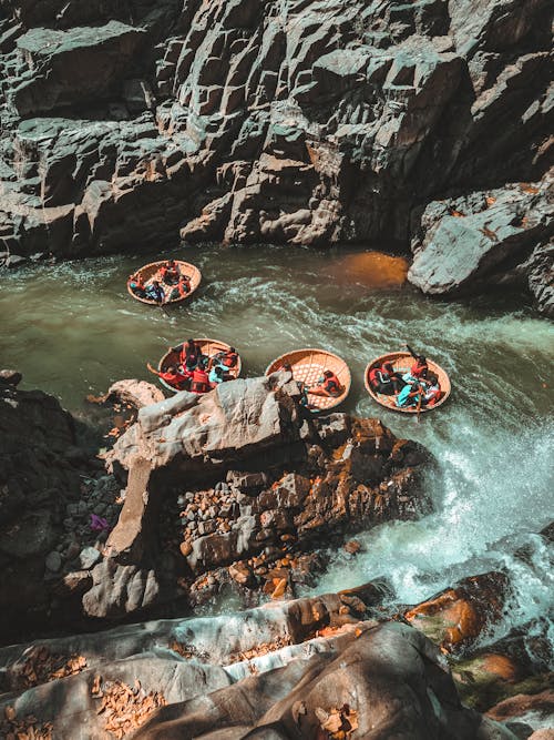 Free From above fearless men floating on typical Vietnamese round fishing boats along fast curvy mountain river between rocky cliffs Stock Photo