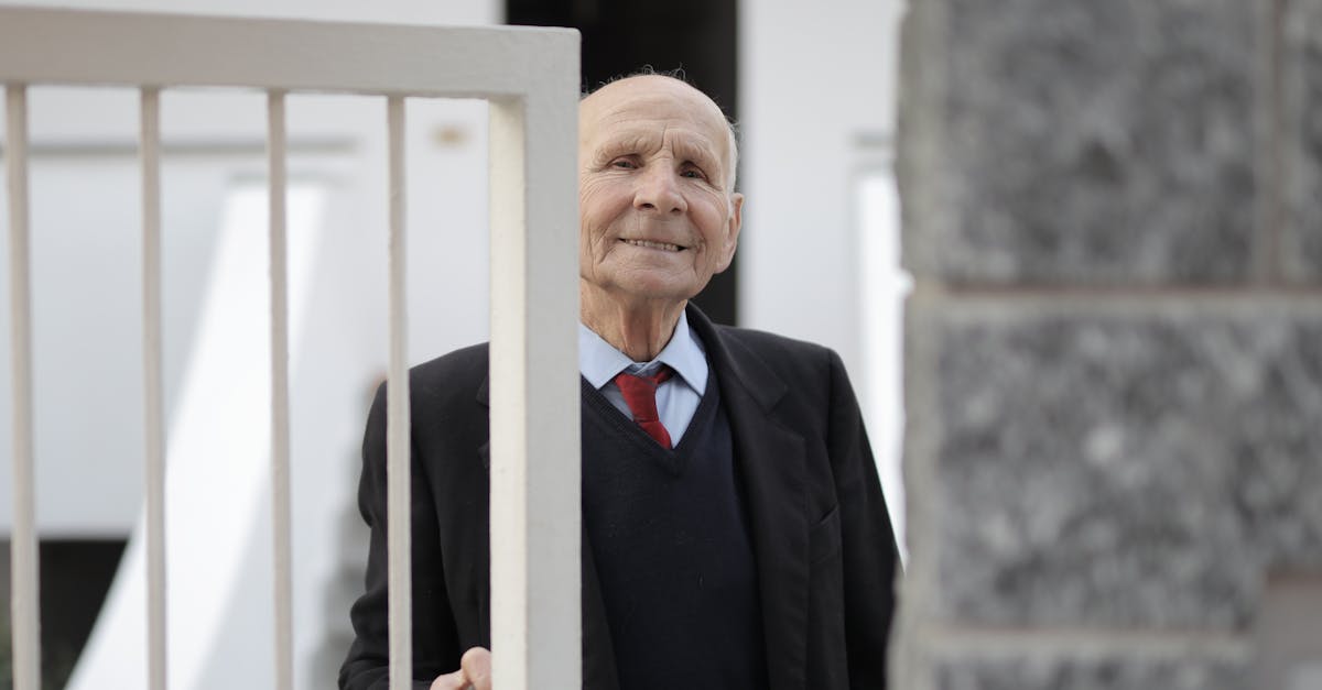 Cheerful elderly man in a suit smiling beside an open gate, outdoors.