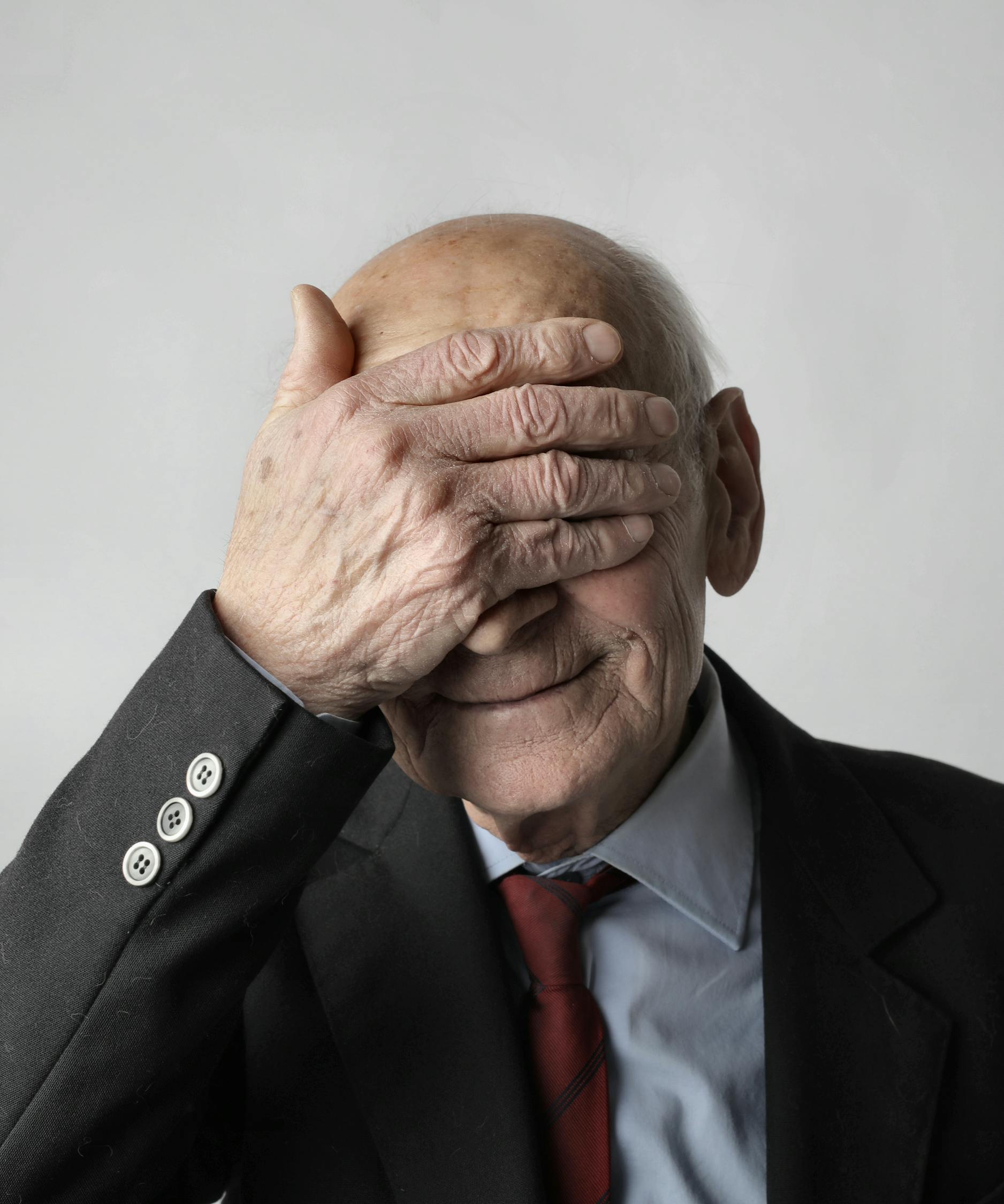 Elderly Man in Black Suit Jacket Covering His Eyes with His Hand