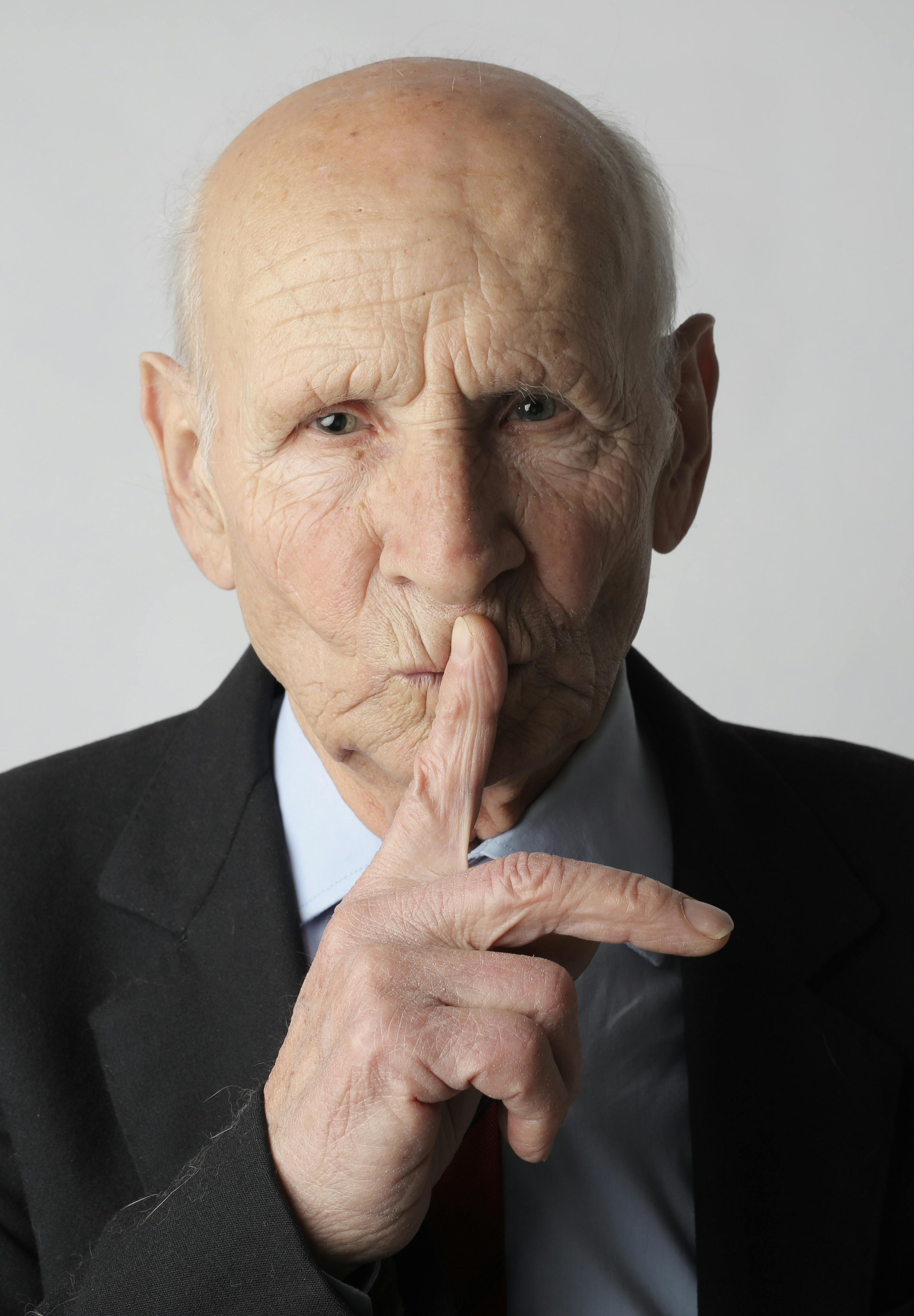 elderly gentleman making silence gesture in studio