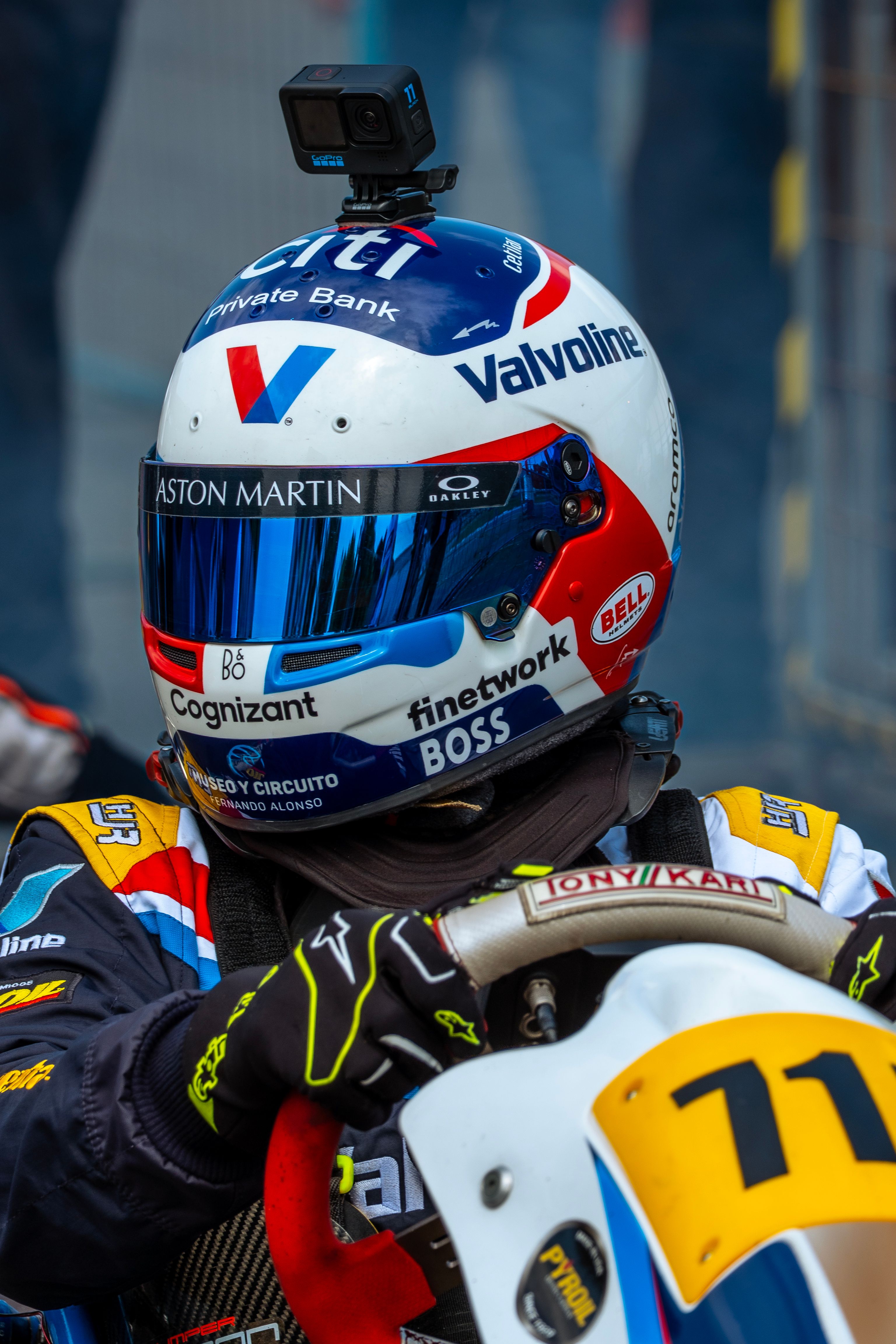 Helmeted kart racer ready for action, showcasing sponsorship logos in a competitive setting.