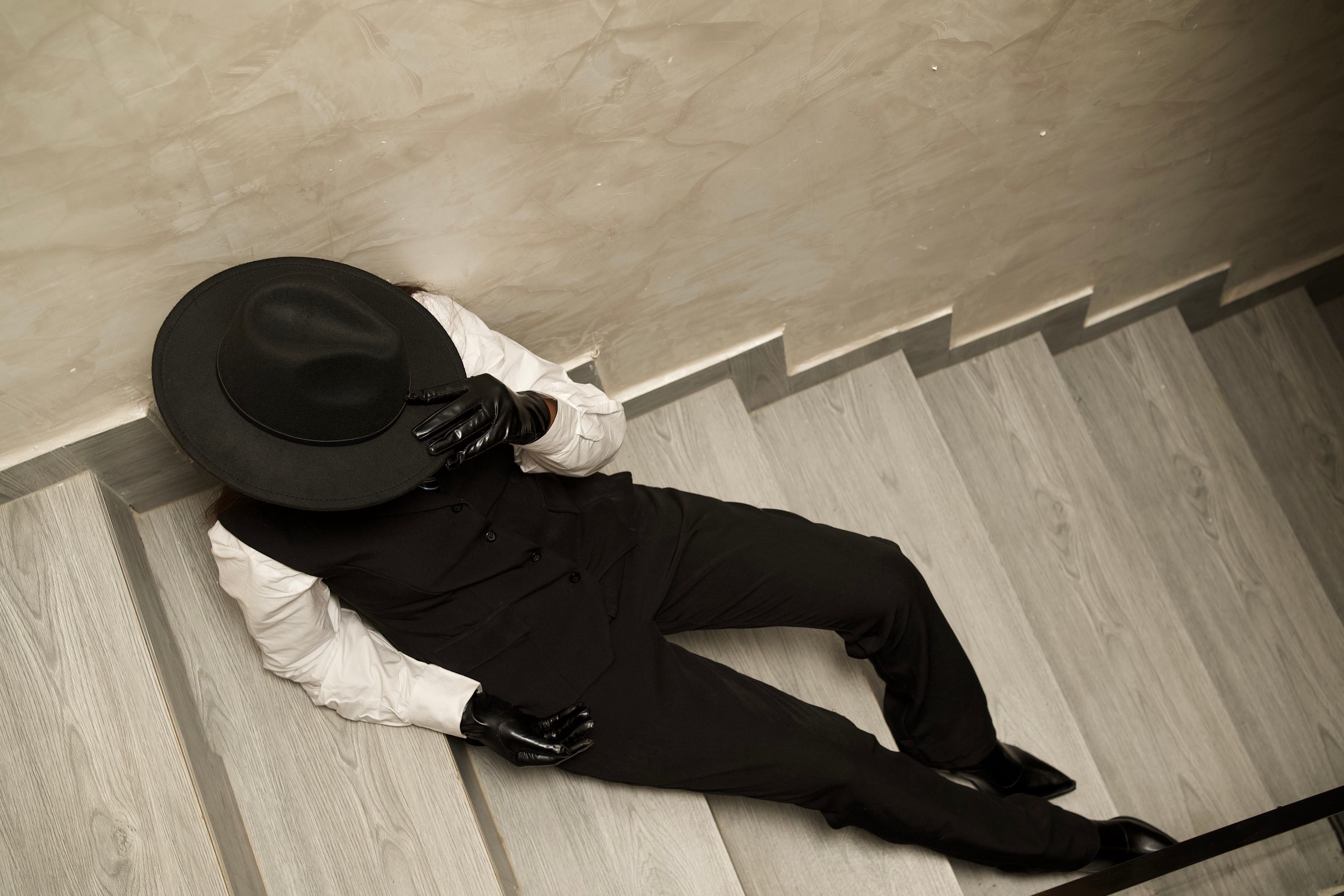 Stylish woman in formal attire with fedora and gloves lounging on stairs, exuding sophistication and elegance.
