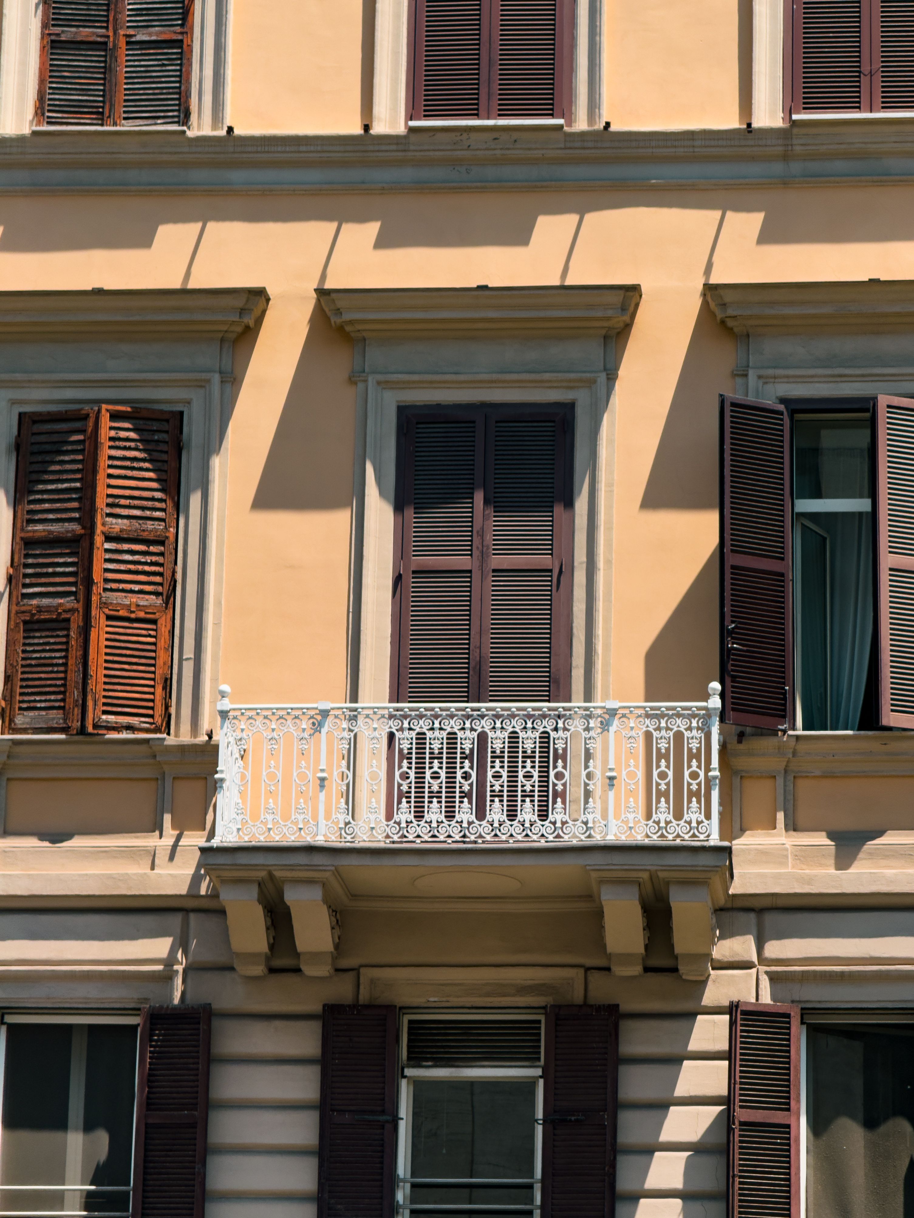 Elegant historic building facade with ornate balcony and wooden shutters under bright daylight.