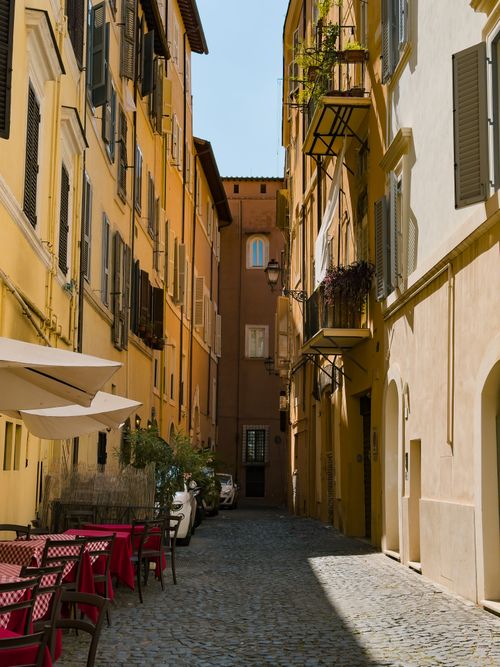 Free Narrow cobblestone alley with colorful buildings and outdoor seating in a sunlit Italian cityscape. Stock Photo