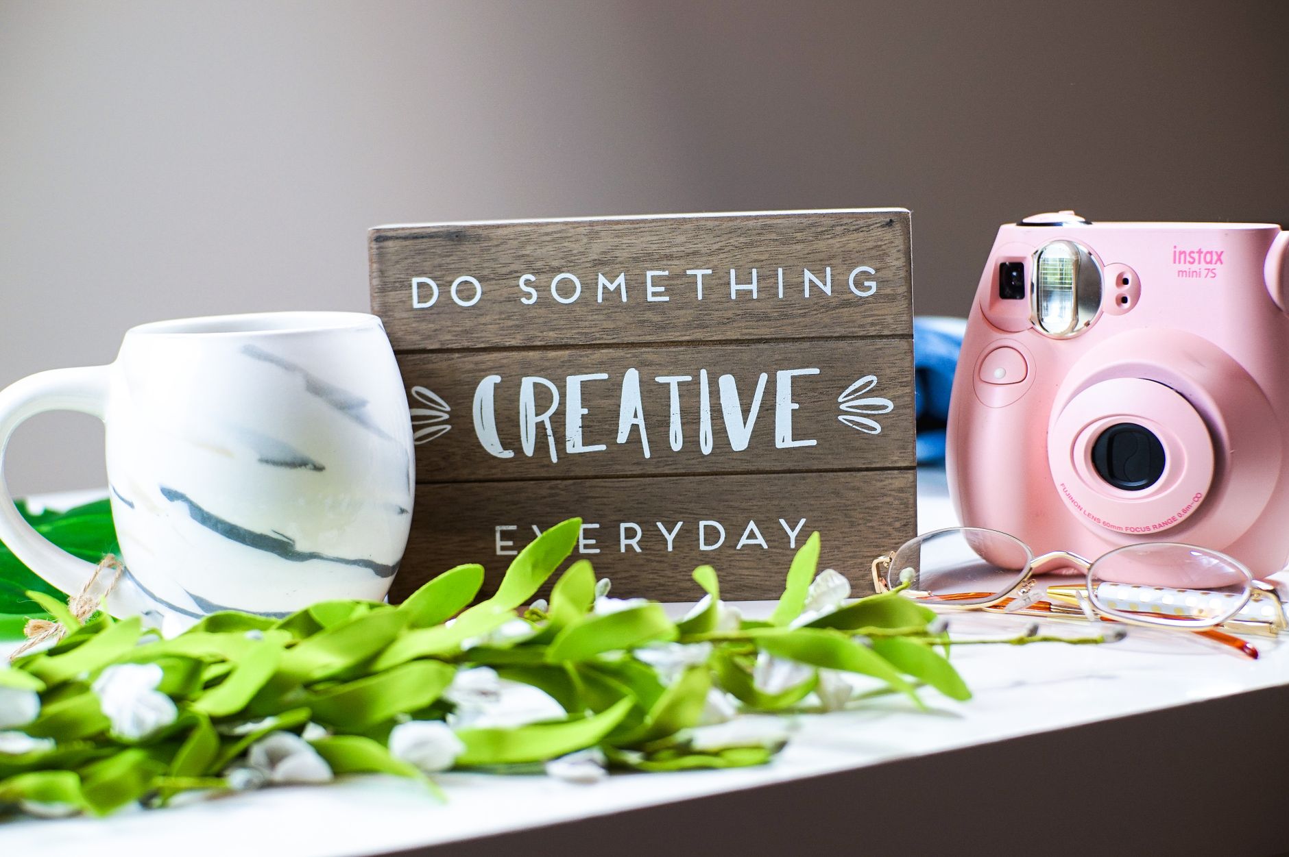 A creative workspace setup featuring a coffee mug, instant camera, and motivational quote.