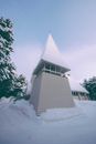 白色创意三角形塔位于冬季乡村雪谷中舒适小屋的旁边