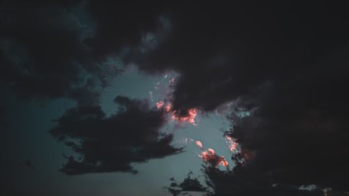 Free From below of black fluffy clouds with pink gleams of setting sun in dark sky Stock Photo