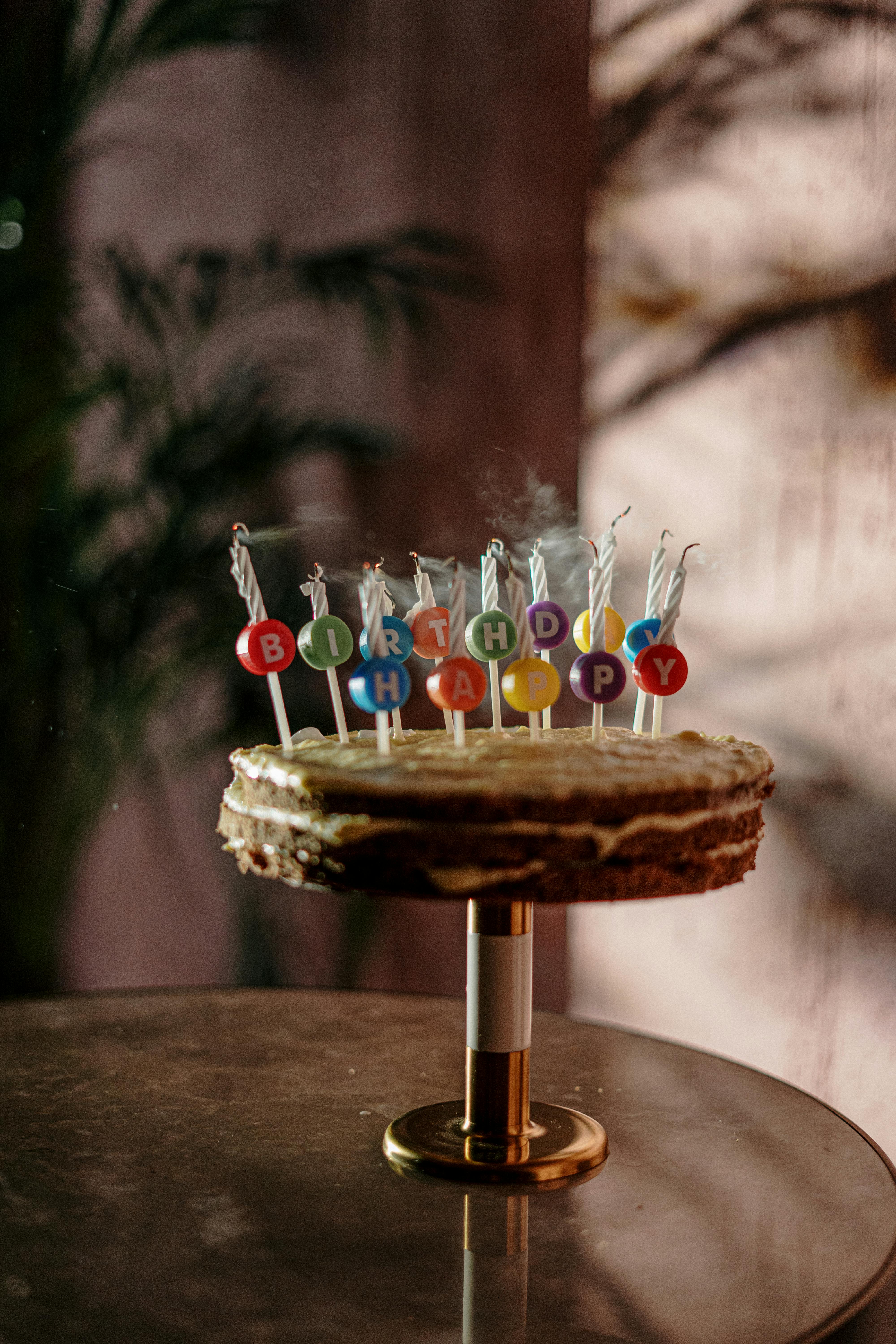 A rustic birthday cake topped with colorful 'Happy Birthday' candles on a table.