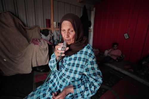 Free An elderly Middle Eastern woman using an inhaler inside a modest home. Emotionally evocative scene. Stock Photo