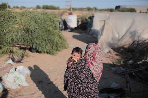 Free Mother carrying child through sandy outdoor area in Gaza. Stock Photo