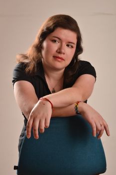 Woman posing with a thoughtful expression, leaning on a blue chair indoors.