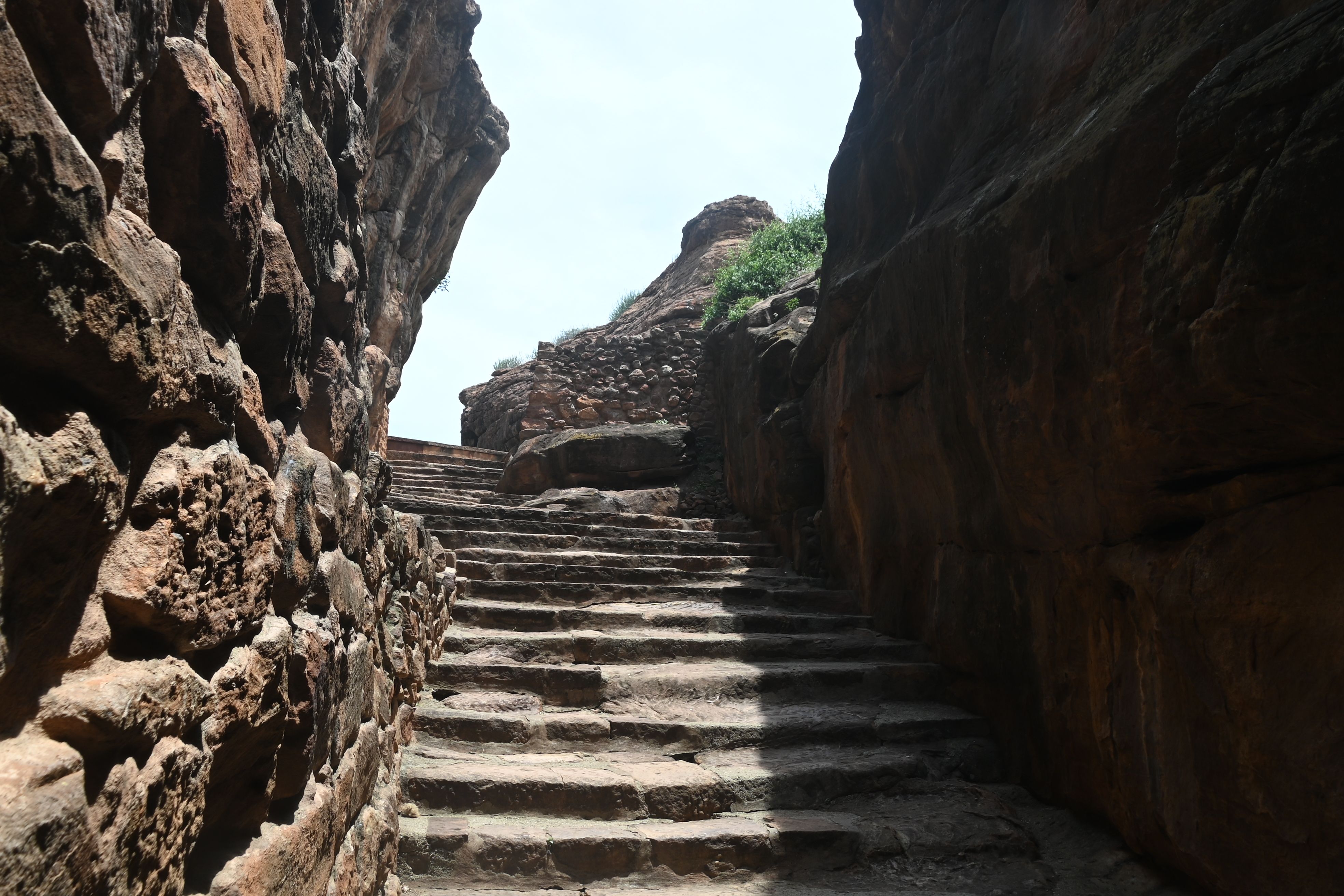 Explore an ancient stone stairway through a sunlit rocky canyon, revealing historical architecture.