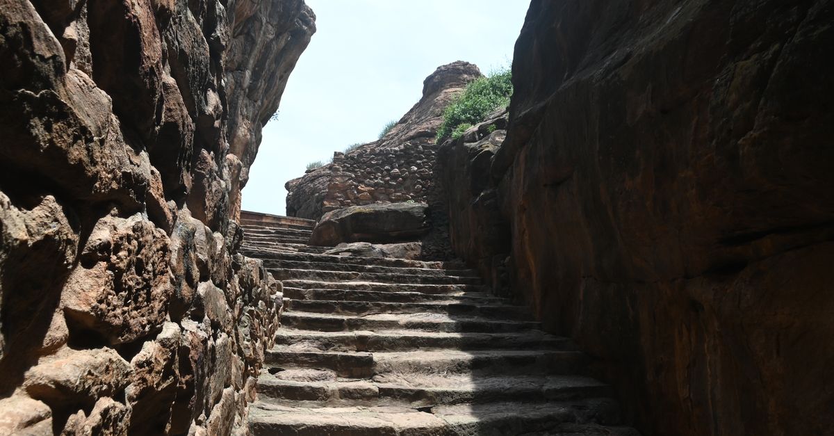 Explore an ancient stone stairway through a sunlit rocky canyon, revealing historical architecture.