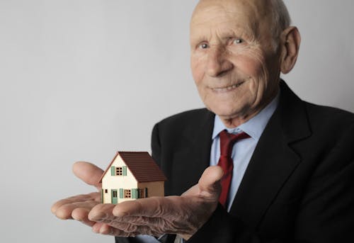 Man in Black Suit Holding Miniature House