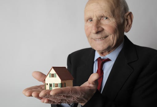 Photo by Andrea Piacquadio Elderly man in business attire holding a small house model, symbolizing real estate investment.