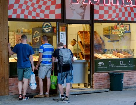 Three adults waiting outside a pizza shop with neon signs at twilight.