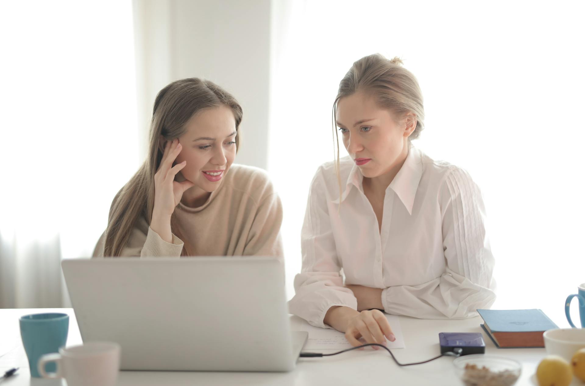 Female workers in casual outfit sitting together at table in bright workplace and thinking of business strategy